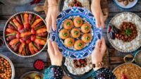 Family dinner with many foods on the table and dessert at the hands of two woman. Local desserts named şekerpare and kemalpaşa tatlısı.